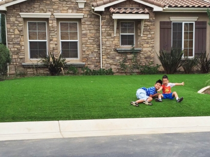 Artificial grass synthetic turf drought water children front yard playing two boys summer green grass lawn gray stone house