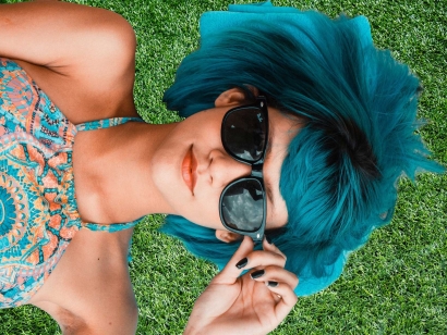 Beautiful woman in dark glasses with blue hair on artificial grass relax