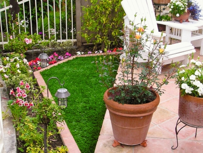 Small backyard area with artificial grass, potted plants, and flower bed